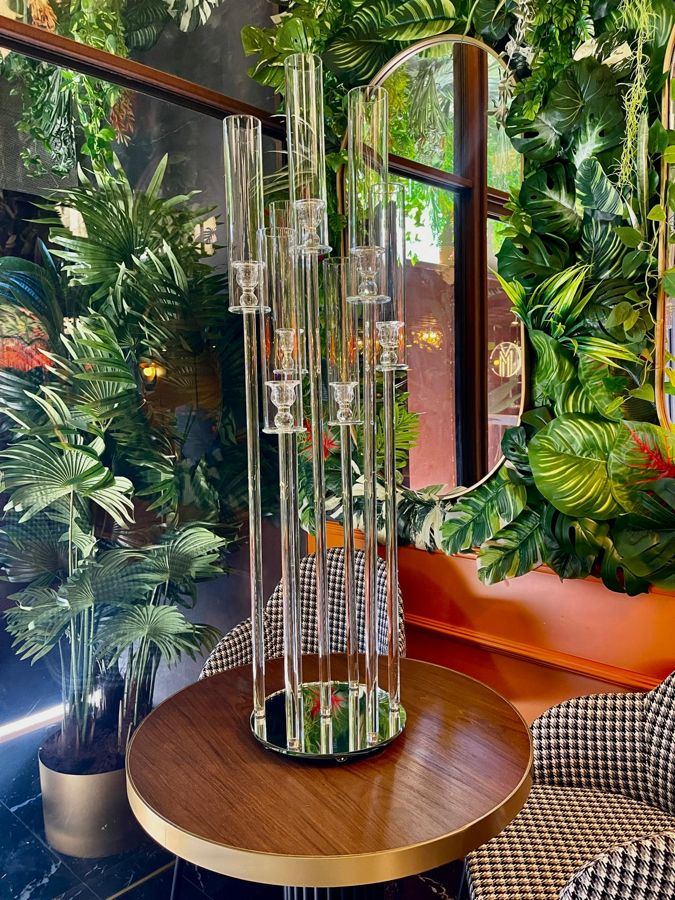 Candelabro in cristallo a piu' steli accanto a una parete vegetale